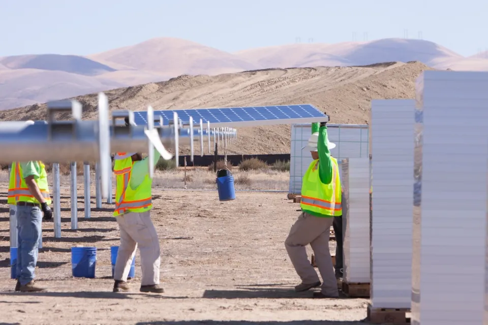 Workers in safety vests installing large solar panels in Southern California desert landscape.